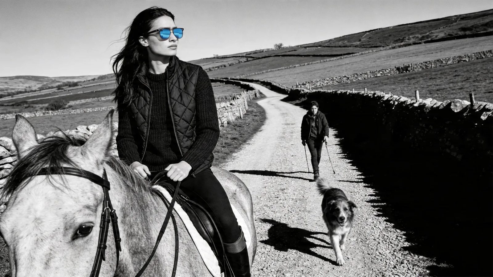 A rider on a dales lane wearing HINDSIGHT rear-view mirror sunglasses — the walker behind visible in the lens, the horse stays calm.