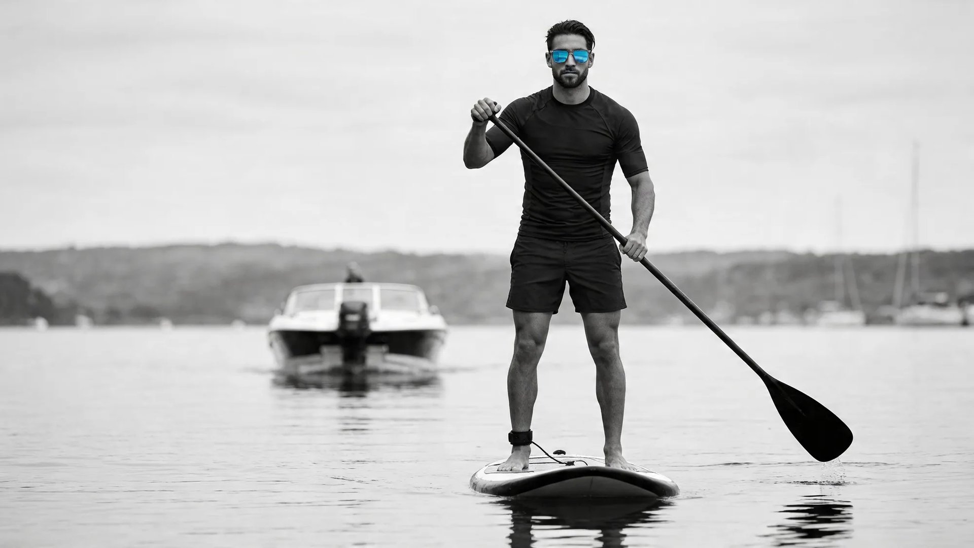 A stand-up paddleboarder on open water wearing HINDSIGHT rear-view mirror sunglasses — the motorboat behind held in the lens.
